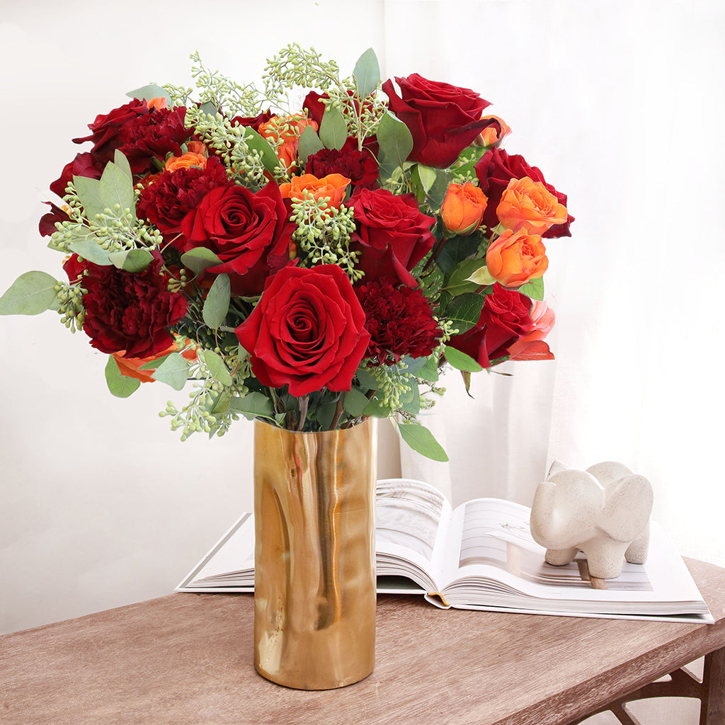 Bouquet of premium red freedom roses carnations and orange spray roses with seeded eucalyptus greeneries.
